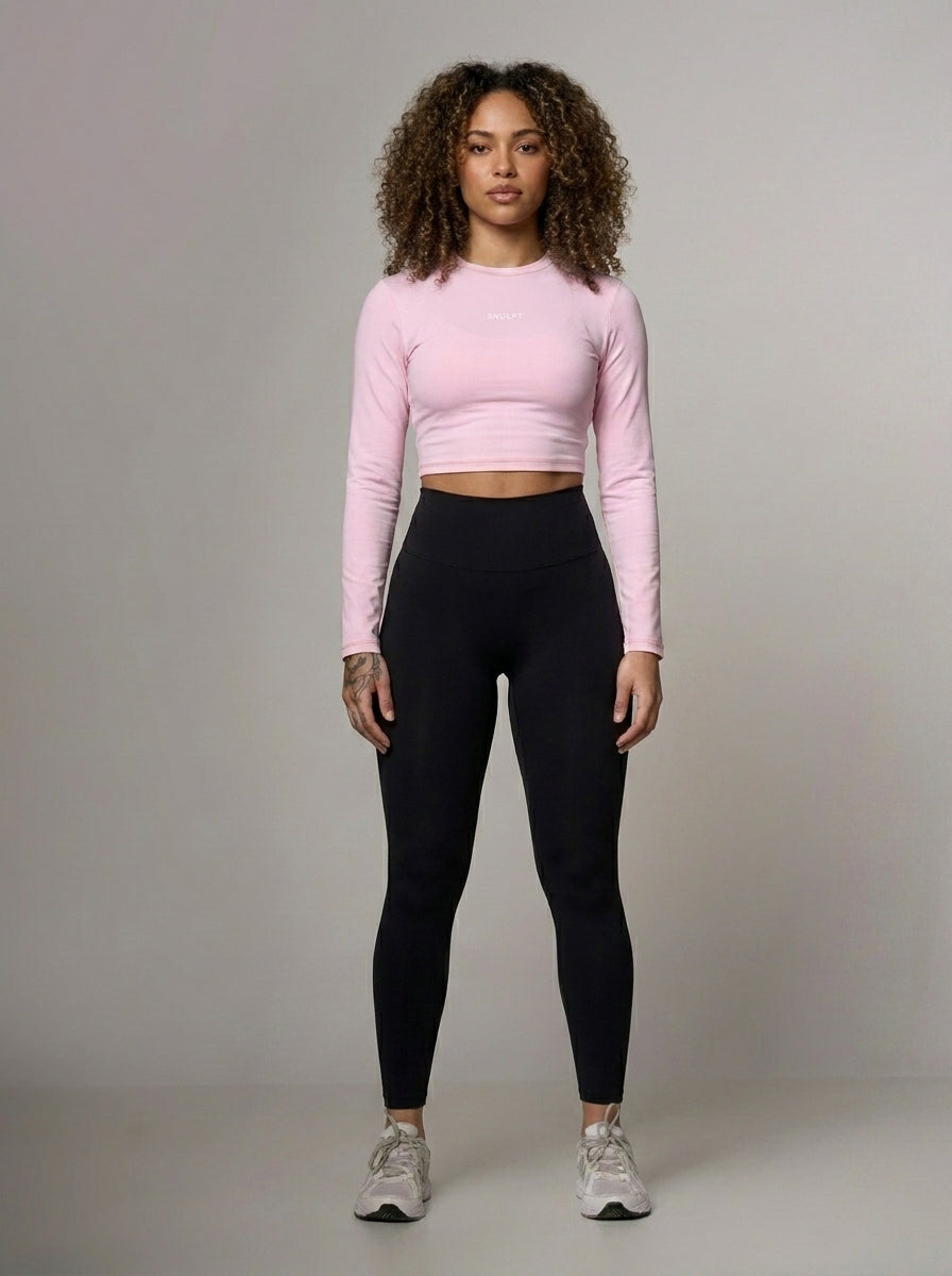 Woman wearing a pink long-sleeve crop top and black leggings against a gray background