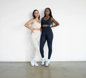 Two women posing together wearing athletic wear against a white background